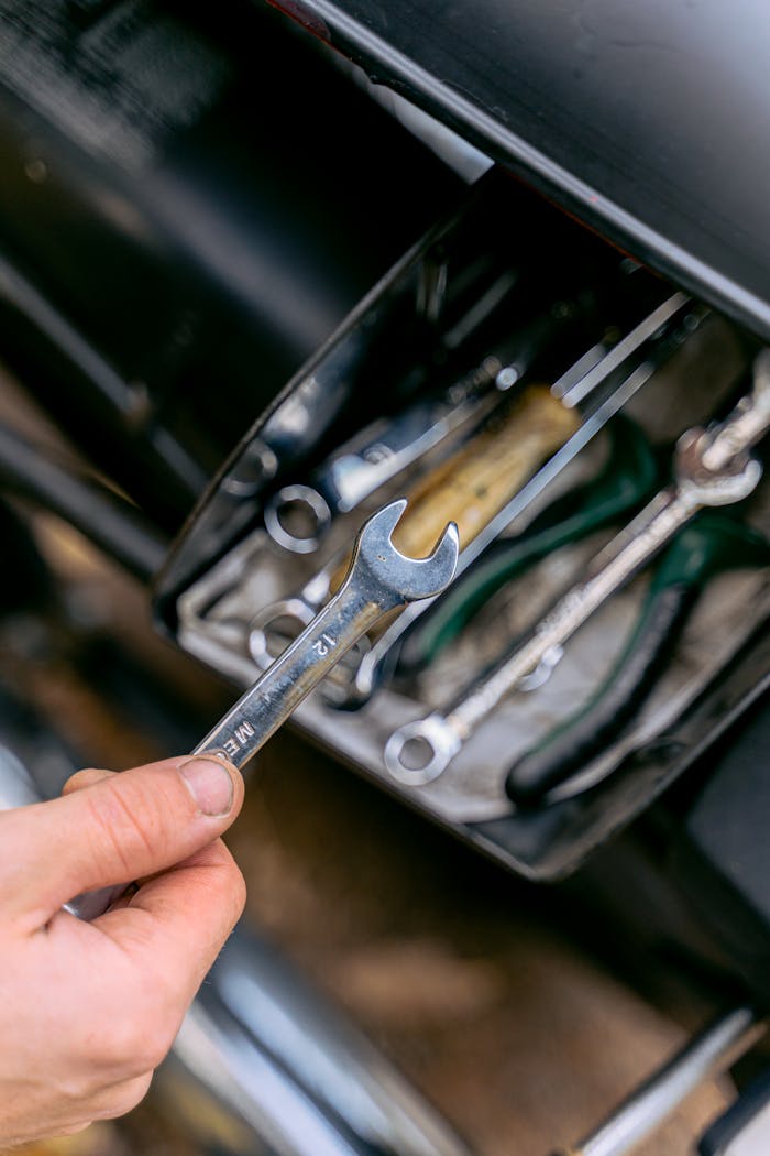 Close-up of a hand holding a metal wrench in front of an open tool box.